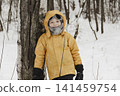 A child in a yellow jacket and gray hat plays in a winter park. A snowy winter forest, a fairy tale. An active, healthy lifestyle and fun games in the snow during the holidays 141459754