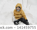 A child in a yellow jacket and gray hat plays in a winter park. A snowy winter forest, a fairy tale. An active, healthy lifestyle and fun games in the snow during the holidays 141459755