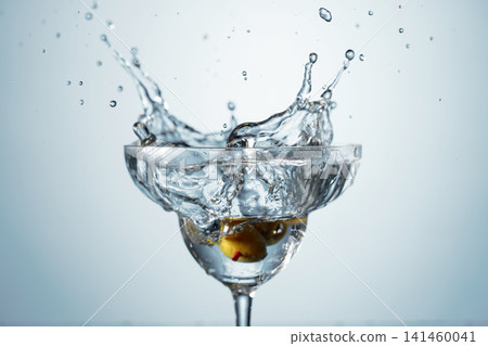 A green olives drops into a martini glass, creating a beautiful splash. A green olives drops into a martini glass, creating a beautiful splash. 141460041
