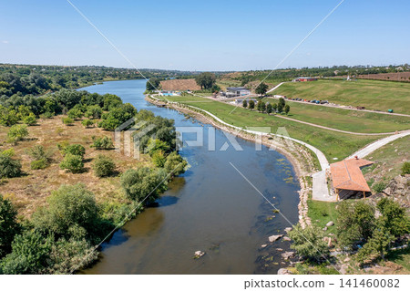 River flows gently beside green trees and open land in the countryside during a sunny day River flows gently beside green trees and open land in the countryside during a sunny day 141460082