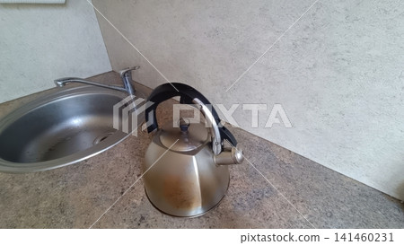 Stainless steel whistling kettle with black handle resting on a speckled countertop beside a kitchen sink and chrome faucet.. Stainless steel whistling kettle with black handle resting on a speckled countertop beside a kitchen sink and chrome faucet.. 141460231
