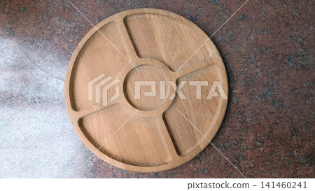 Round wooden serving tray with five compartments, centered on a mottled brown and gray textured surface, eye level view.. Round wooden serving tray with five compartments, centered on a mottled brown and gray textured surface, eye level view.. 141460241