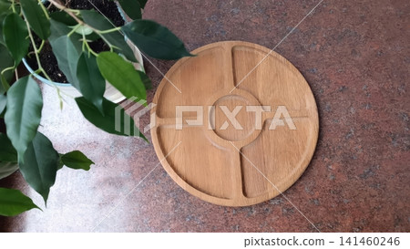 Round wooden serving tray with five compartments on speckled red black countertop, green plant leaves visible in the top left corner.. 141460246