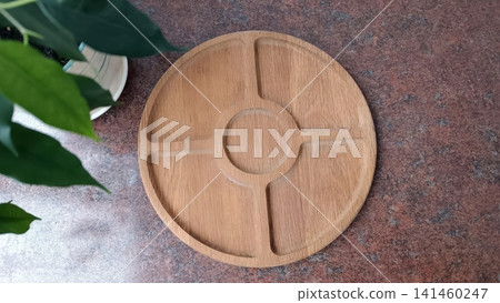 Light brown wooden serving tray with five compartments on a dark red brown textured surface, houseplant leaves in top corner.. 141460247