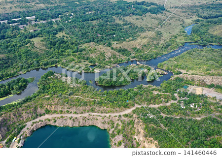 Aerial view of a winding river flowing through green hills, surrounded by trees and rocks, with some clear water bodies under a bright sky Aerial view of a winding river flowing through green hills, surrounded by trees and rocks, with some clear water bodies under a bright sky 141460446