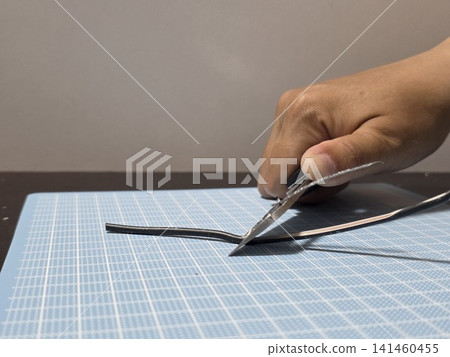 DIY and electrical work practice: A hand using a utility knife to strip the sheath from a VVF cable. DIY and electrical work practice: A hand using a utility knife to strip the sheath from a VVF cable. 141460455