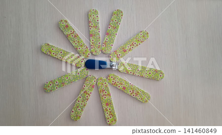 Blue nail clipper surrounded by floral patterned nail files arranged like flower petals on a light wooden surface. 141460849
