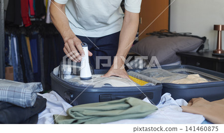 a man compresses clothes in a vacuum storage bag a man compresses clothes in a vacuum storage bag 141460875