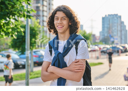 Smiling teenage student with curly hair and backpack standing on the city street 141462628