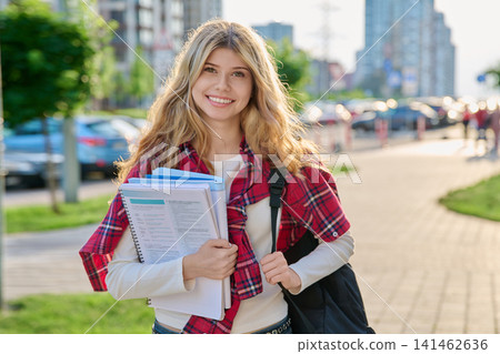 Happy female student with backpack and textbooks standing outside 141462636