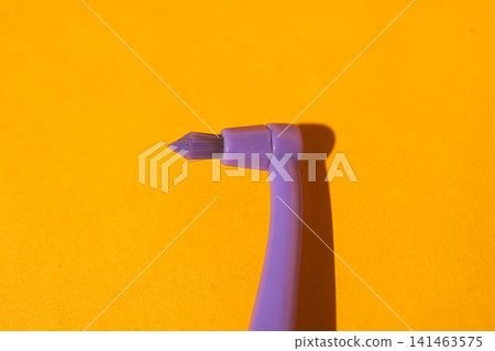 Purple paintbrush with angled tip resting on a vibrant yellow background, showcasing the brush's bristles and ergonomic handle design for artistic use Purple paintbrush with angled tip resting on a vibrant yellow background, showcasing the brush's bristles and ergonomic handle design for artistic use 141463575