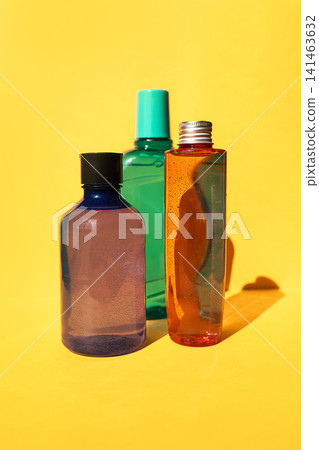 Three colorful plastic bottles with varying shapes and sizes, featuring a purple, green, and orange hue, placed against a bright yellow background Three colorful plastic bottles with varying shapes and sizes, featuring a purple, green, and orange hue, placed against a bright yellow background 141463632