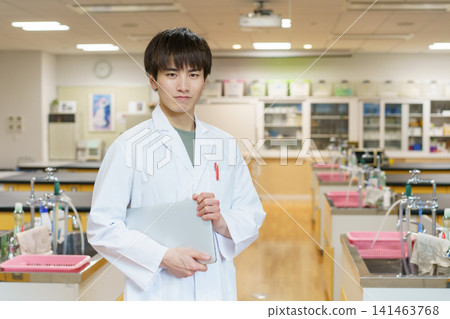 Portrait of a young male researcher standing with a laptop computer. Photography assistance provided by: Denpa Gakuen Educational Foundation, Tokyo Electronics College. 141463768