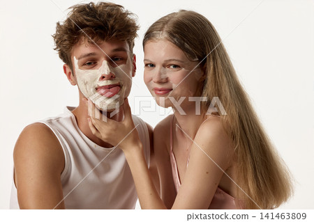 Confident young couple posing together while man wears cleansing face mask Confident young couple posing together while man wears cleansing face mask 141463809
