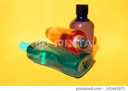Three colorful plastic bottles of different shapes and sizes arranged on a bright yellow background, showcasing various container designs for personal care products Three colorful plastic bottles of different shapes and sizes arranged on a bright yellow background, showcasing various container designs for personal care products 141463873