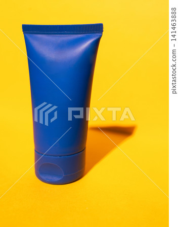 Blue plastic tube container for cream or lotion on a vibrant yellow background, showcasing a clean and modern design suitable for cosmetic packaging Blue plastic tube container for cream or lotion on a vibrant yellow background, showcasing a clean and modern design suitable for cosmetic packaging 141463888