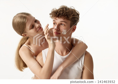 Affectionate young woman hugging boyfriend while applying cream beneath eye Affectionate young woman hugging boyfriend while applying cream beneath eye 141463932