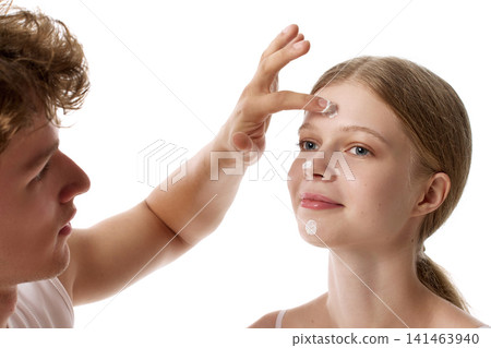 Calm blonde young woman receiving sunscreen on forehead from male partner Calm blonde young woman receiving sunscreen on forehead from male partner 141463940