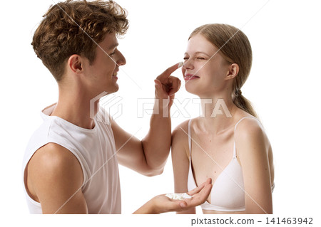 Caring young man applying sunscreen to smiling woman nose in profile view Caring young man applying sunscreen to smiling woman nose in profile view 141463942