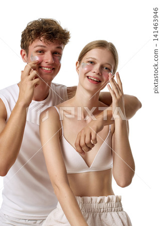 Playful fair-skinned young couple applying facial cream and smiling at camera Playful fair-skinned young couple applying facial cream and smiling at camera 141463946