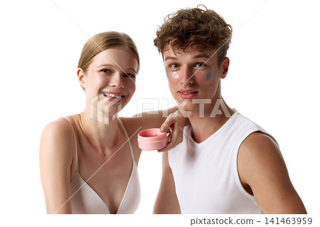 Cheerful young couple presenting pink skincare jar against white background 141463959