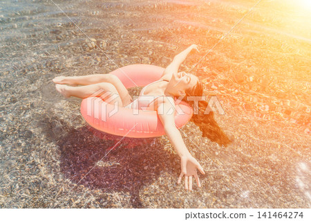 Woman swimming tube happy young woman floats in a pink inflatable ring on clear sea water during a golden sunset Woman swimming tube happy young woman floats in a pink inflatable ring on clear sea water during a golden sunset 141464274