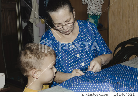 gentle grandmother blue top patiently shows her young grandson how sew piece fabric focused collaboration capturing warmth family learning passing traditions quiet joy creating something together gentle grandmother blue top patiently shows her young grandson how sew piece fabric focused collaboration capturing warmth family learning passing traditions quiet joy creating something together 141464521