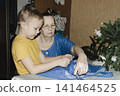 gentle grandmother blue top patiently shows her young grandson how sew piece fabric focused collaboration capturing warmth family learning passing traditions quiet joy creating something together 141464525