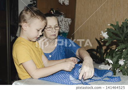gentle grandmother blue top patiently shows her young grandson how sew piece fabric focused collaboration capturing warmth family learning passing traditions quiet joy creating something together gentle grandmother blue top patiently shows her young grandson how sew piece fabric focused collaboration capturing warmth family learning passing traditions quiet joy creating something together 141464525
