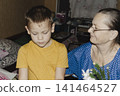 gentle grandmother blue top patiently shows her young grandson how sew piece fabric focused collaboration capturing warmth family learning passing traditions quiet joy creating something together 141464527