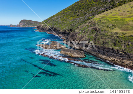 Aerial view of the clear turquoise waters surrounding Blueys Head at Blueys Beach, with the rocky headland, pristine sandy shoreline and vibrant coastal waters along the Mid North Coast of NSW. Aerial view of the clear turquoise waters surrounding Blueys Head at Blueys Beach, with the rocky headland, pristine sandy shoreline and vibrant coastal waters along the Mid North Coast of NSW. 141465178