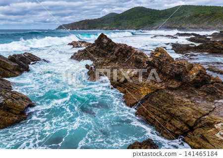 Aerial view of powerful waves breaking across rugged rock formations, creating swirling whitewash along the coastline at Burgess Beach, Forster on the Mid North Coast of NSW. Aerial view of powerful waves breaking across rugged rock formations, creating swirling whitewash along the coastline at Burgess Beach, Forster on the Mid North Coast of NSW. 141465184