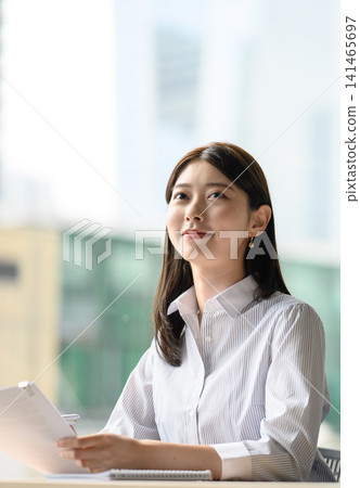A young woman looks up at the sky while looking at documents. A young woman looks up at the sky while looking at documents. 141465697