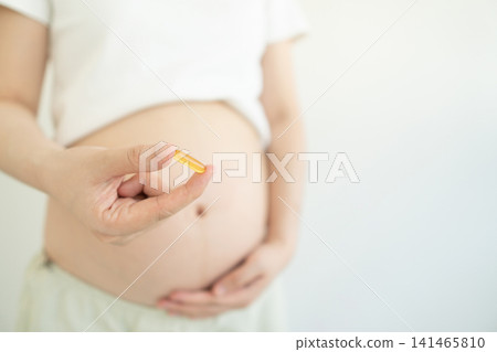 Pregnant woman holding dietary supplement capsule against white background. Omega 3 fatty acid DHA to support a healthy pregnancy and development of baby's brain and nervous system. Maternity prenatal Pregnant woman holding dietary supplement capsule against white background. Omega 3 fatty acid DHA to support a healthy pregnancy and development of baby's brain and nervous system. Maternity prenatal 141465810