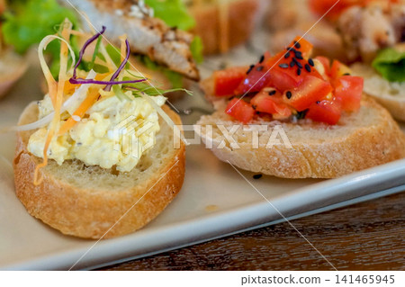 Assorted open sandwiches with egg salad and tomato bruschetta on toasted bread, appetizer platter close up, gourmet cafe style finger food with selective focus 141465945