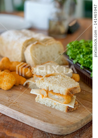 Homemade chicken nugget cheese sandwich on wooden board with fresh microgreens background, close up soft natural lighting, simple quick meal concept Homemade chicken nugget cheese sandwich on wooden board with fresh microgreens background, close up soft natural lighting, simple quick meal concept 141465947