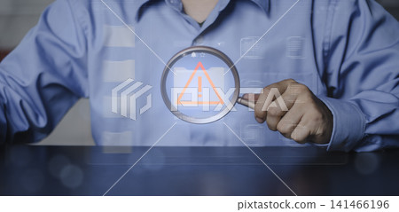 Cybersecurity audit, system vulnerability detection and information technology error inspection. Professional hand holding magnifying glass focusing on warning alert icon inside digital folder. 141466196