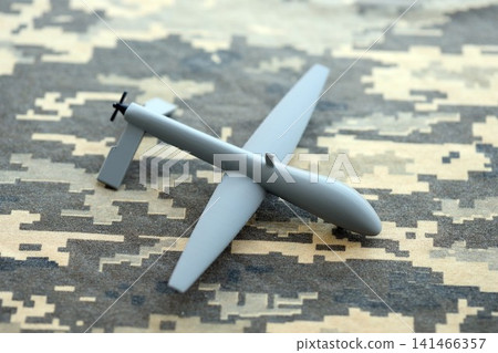 Unnamed grey toy drone model on camouflage fabric. Observation drone for intelligence tasks Unnamed grey toy drone model on camouflage fabric. Observation drone for intelligence tasks 141466357