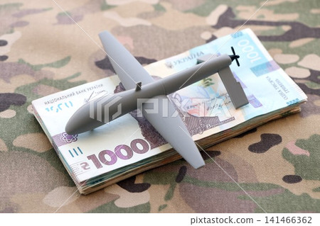 Unnamed grey toy drone and ukrainian money bills on camouflage fabric close up Unnamed grey toy drone and ukrainian money bills on camouflage fabric close up 141466362