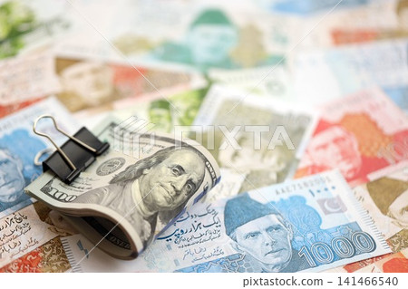 Roll of US dollar bills lies on big amount of Pakistan rupees banknotes close up Roll of US dollar bills lies on big amount of Pakistan rupees banknotes close up 141466540