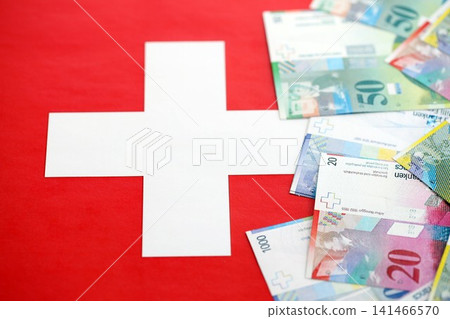 Swiss franc banknotes and flag. The current francs money bills lies on flag in big amount Swiss franc banknotes and flag. The current francs money bills lies on flag in big amount 141466570