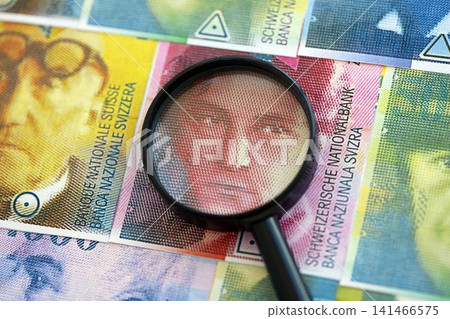 Swiss franc banknotes and magnifying glass. The francs money bills with loupe lies on table Swiss franc banknotes and magnifying glass. The francs money bills with loupe lies on table 141466575