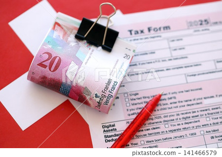 Swiss franc banknotes and tax form with pen. The current francs money bills lies on tax return form Swiss franc banknotes and tax form with pen. The current francs money bills lies on tax return form 141466579
