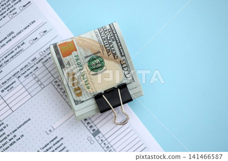 Big amount of United States USD dollar bills on table with 1040 tax return form 141466587