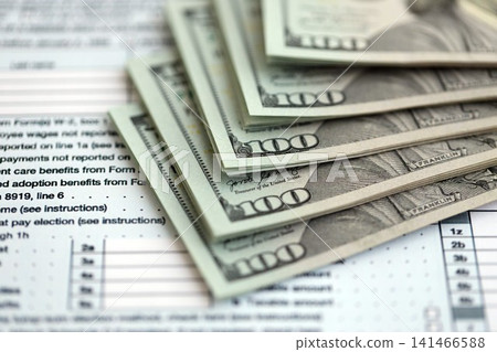 Big amount of United States USD dollar bills banknotes on table with 1040 tax return form Big amount of United States USD dollar bills banknotes on table with 1040 tax return form 141466588