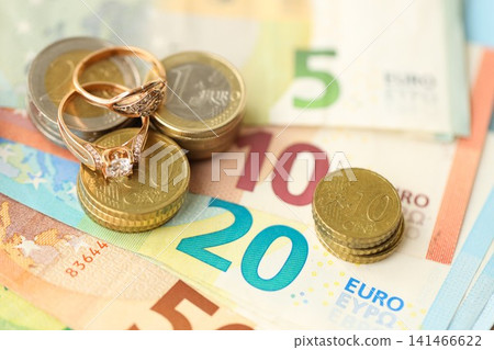 European union Euro money bills and coins with wedding rings on blue table European union Euro money bills and coins with wedding rings on blue table 141466622