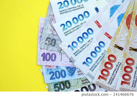 Argentine pesos money bills in big amount lies on yellow color table close up Argentine pesos money bills in big amount lies on yellow color table close up 141466676