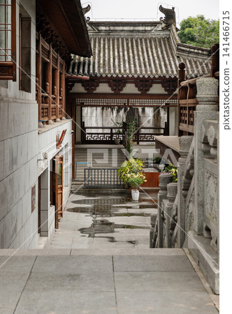 Elegant traditional Chinese architecture frames a serene, rain-kissed pathway leading to the sacred Dazu Rock Carvings. Elegant traditional Chinese architecture frames a serene, rain-kissed pathway leading to the sacred Dazu Rock Carvings. 141466715