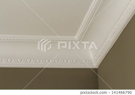 Ornamental white molding decor on ceiling of white room close-up detail. Interior renovation and construction concept. Ornamental white molding decor on ceiling of white room close-up detail. Interior renovation and construction concept. 141466790