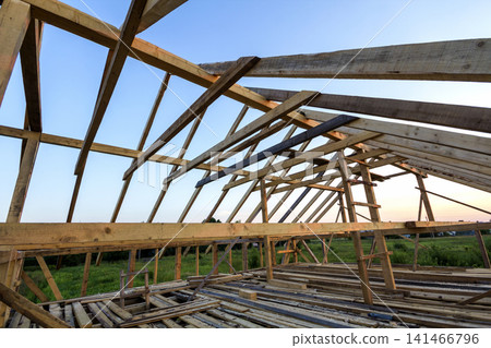 New wooden house under construction. Close-up of attic roof frame against clear sky from inside. Ecological dream home of natural materials. Building, construction and renovation concept. New wooden house under construction. Close-up of attic roof frame against clear sky from inside. Ecological dream home of natural materials. Building, construction and renovation concept. 141466796